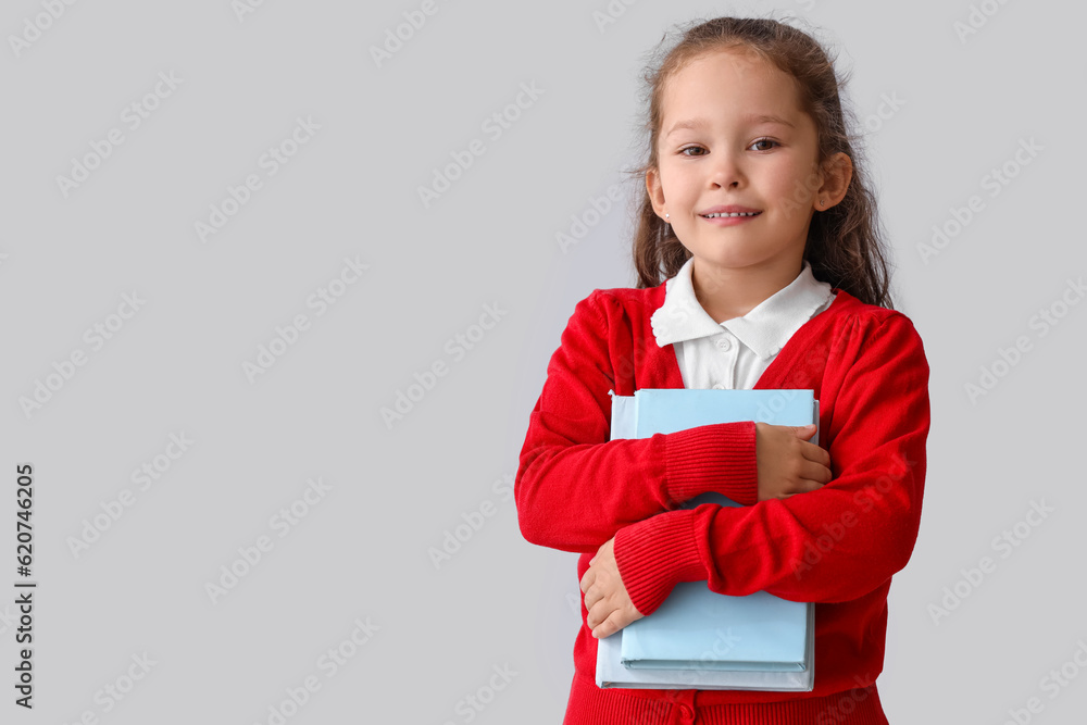 Little schoolgirl with books on grey background