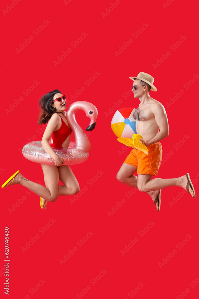 Young couple with beach accessories jumping on red background