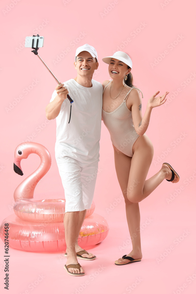 Young couple with inflatable rings taking selfie on pink background