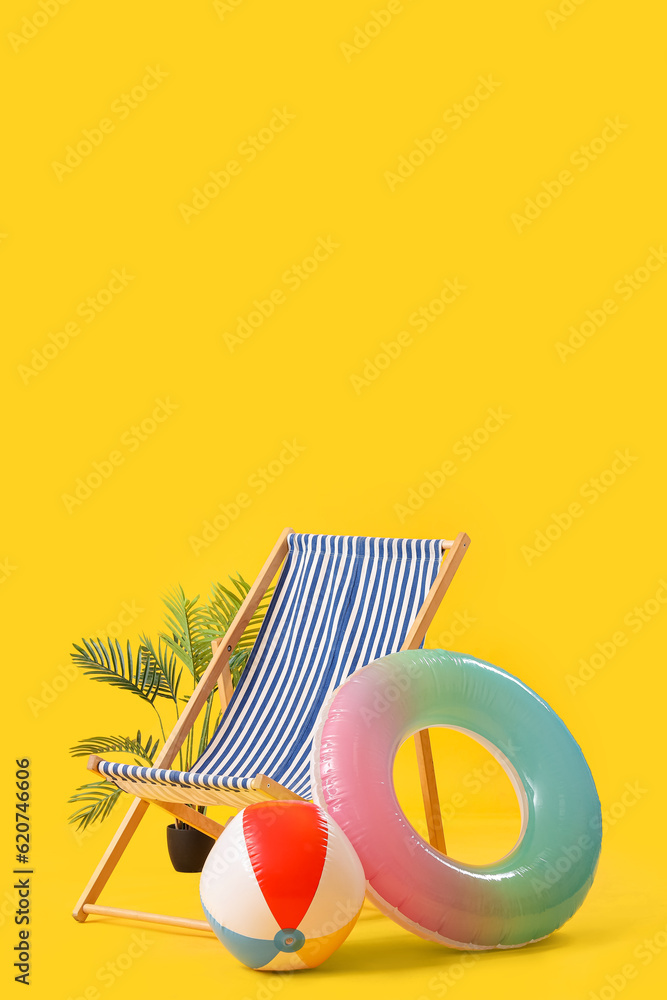 Deck chair with beach ball, inflatable ring and palm tree on yellow background