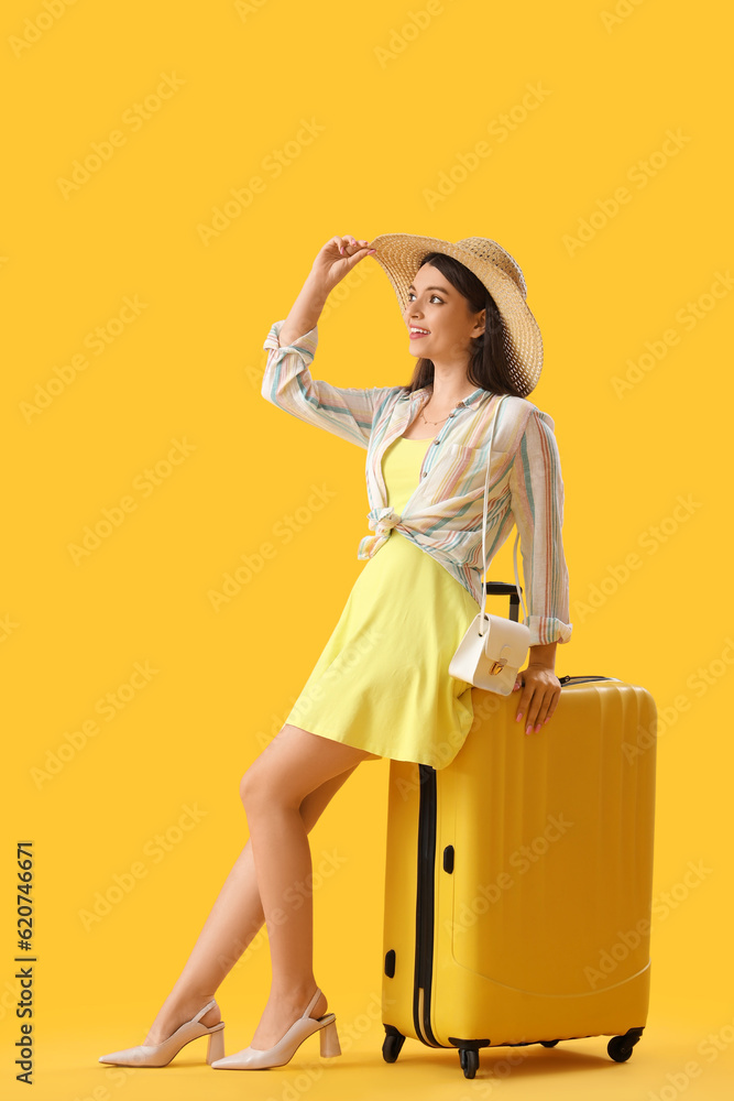 Young woman with suitcase on yellow background