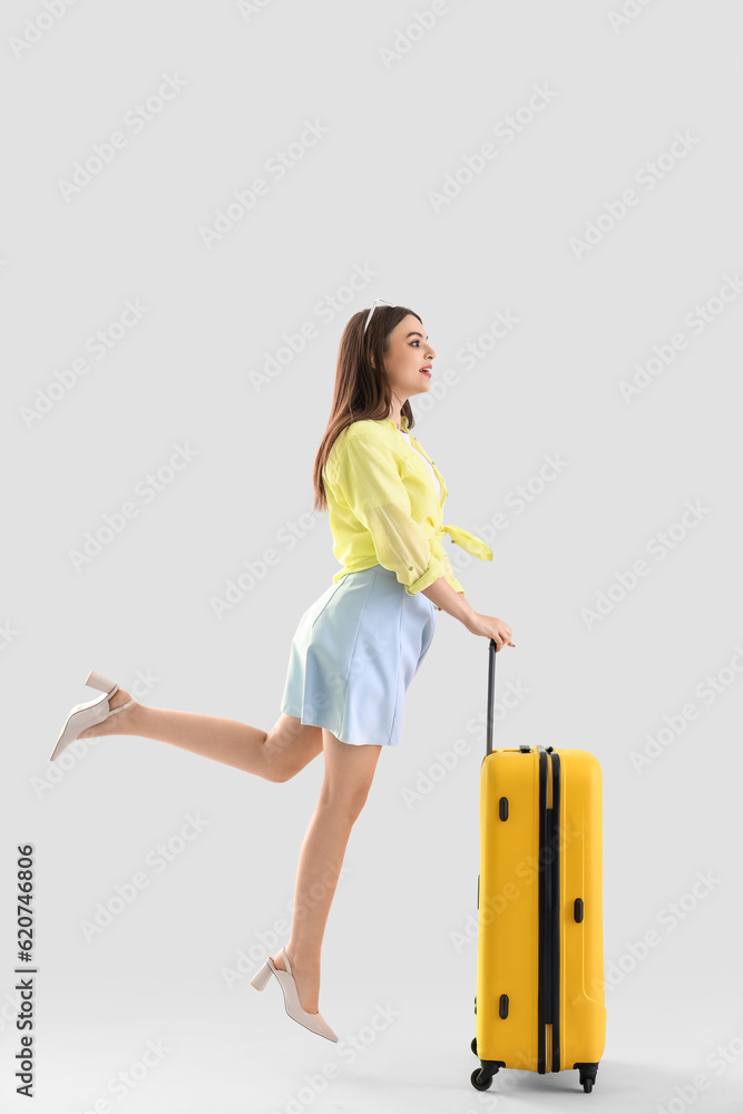 Young woman with suitcase jumping on light background