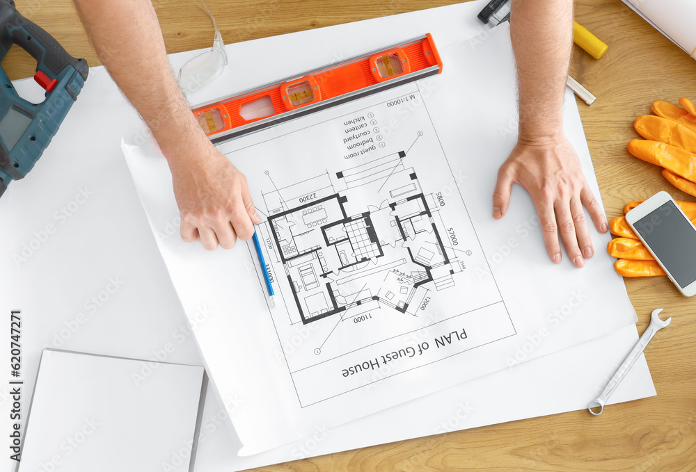 Male builder working with house plan at table in room, top view