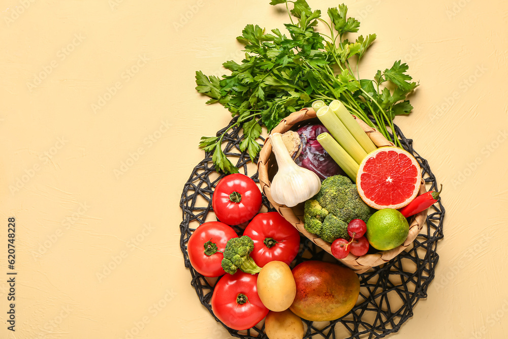 Wicker basket with different fresh fruits and vegetables on yellow background