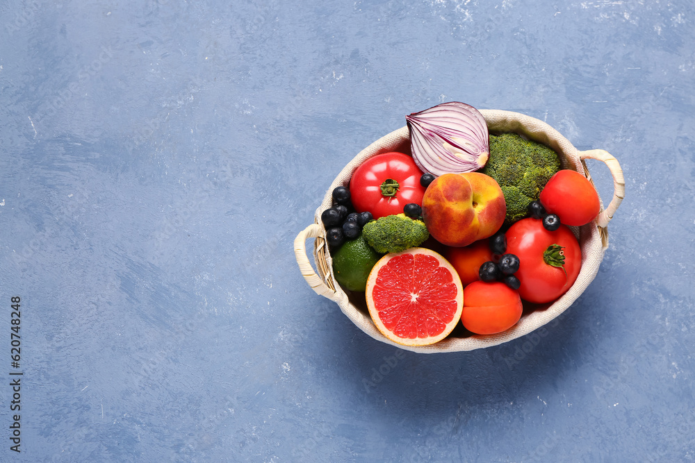 Wicker basket with different fresh fruits and vegetables on blue background