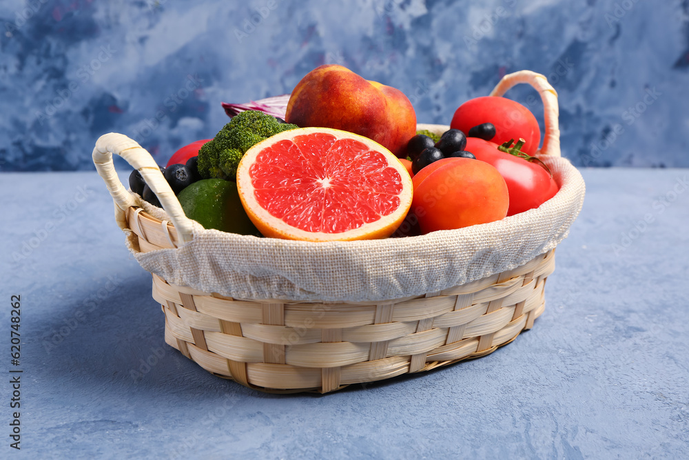 Wicker basket with different fresh fruits and vegetables on blue background