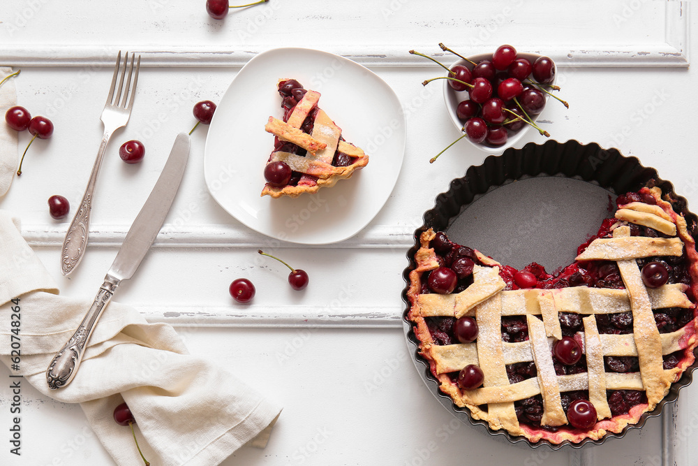 Baking dish with tasty cherry pie and plate of piece on white background