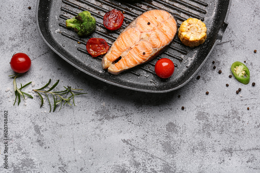 Frying pan with tasty grilled salmon steak and vegetables on grey background