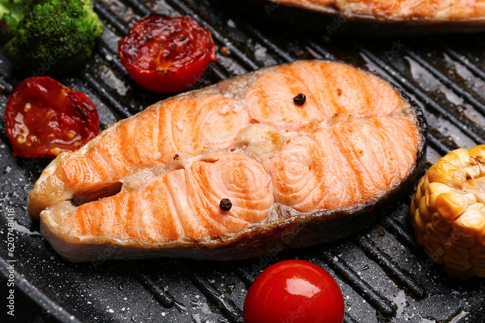 Tasty grilled salmon steak and vegetables in frying pan, closeup