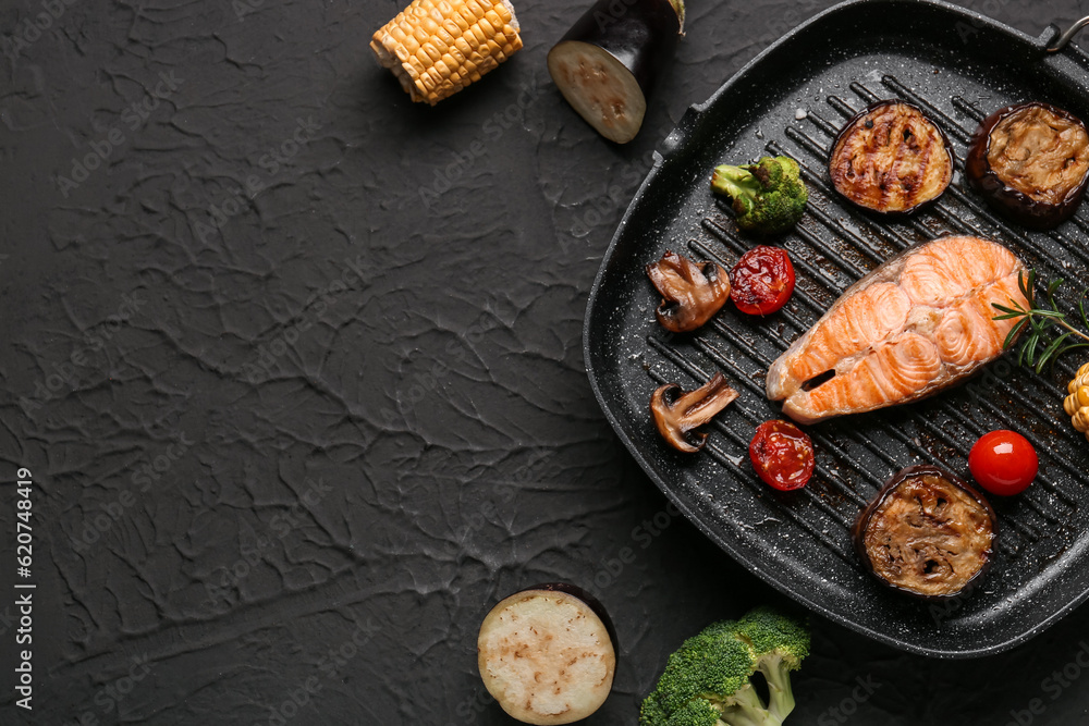 Frying pan with tasty grilled salmon steak and vegetables on black background