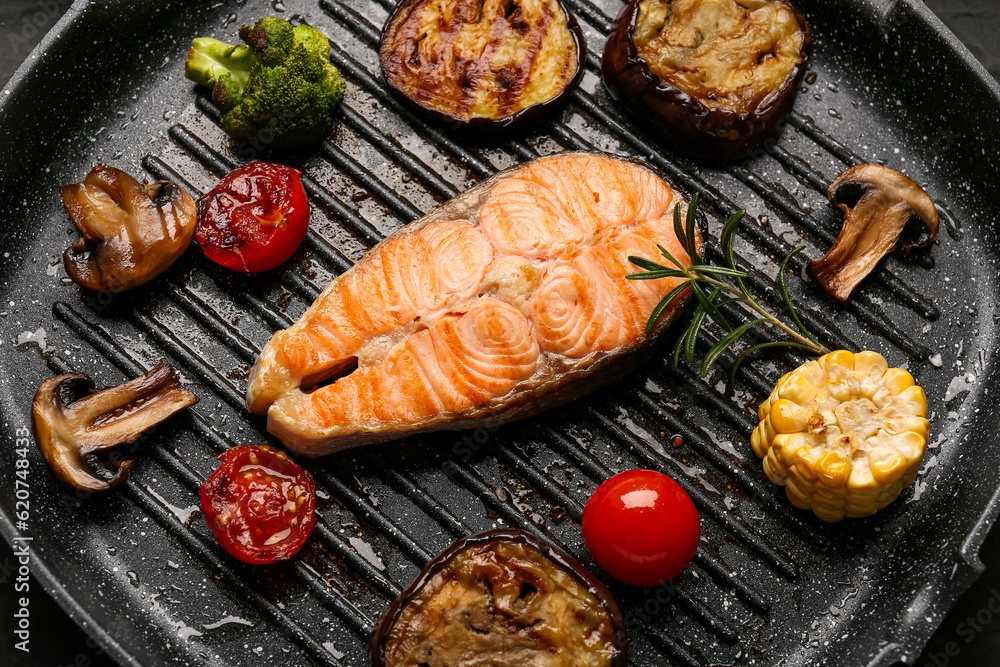 Tasty grilled salmon steak and vegetables in frying pan, closeup