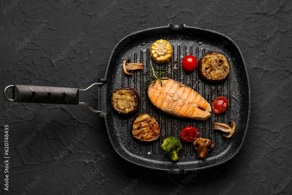 Frying pan with tasty grilled salmon steak and vegetables on black background