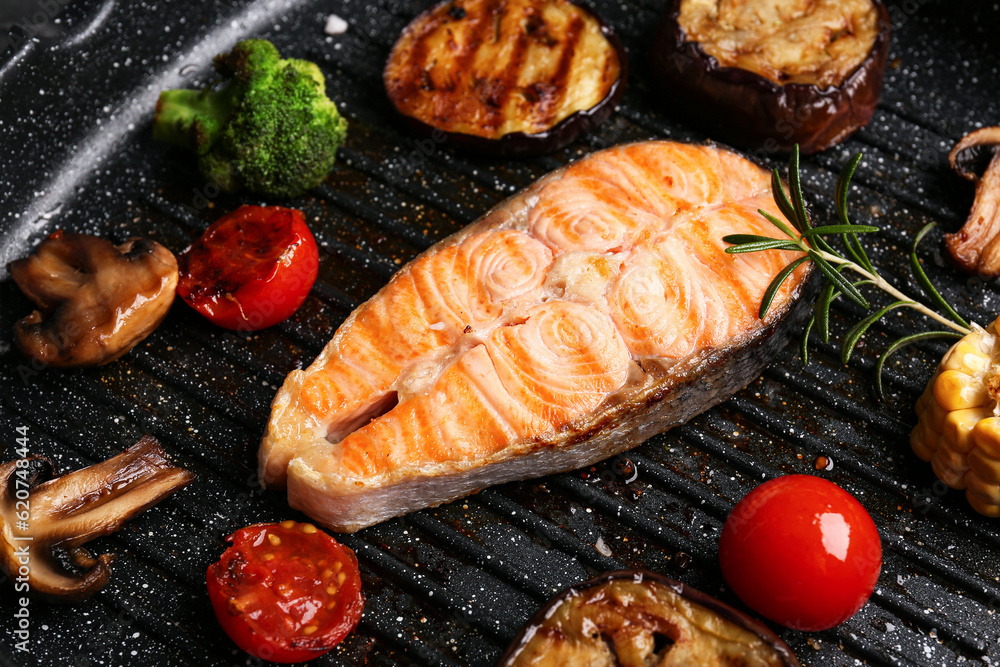 Tasty grilled salmon steak and vegetables in frying pan, closeup