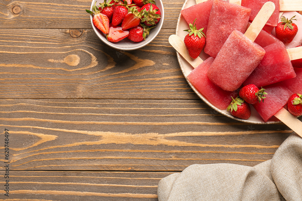 Plate with sweet strawberry ice-cream popsicles and bowl of berries on wooden background