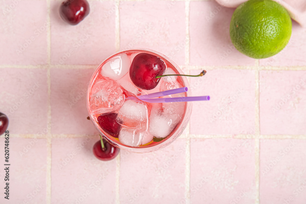 Glass of tasty cherry lemonade and lime on pink tile table