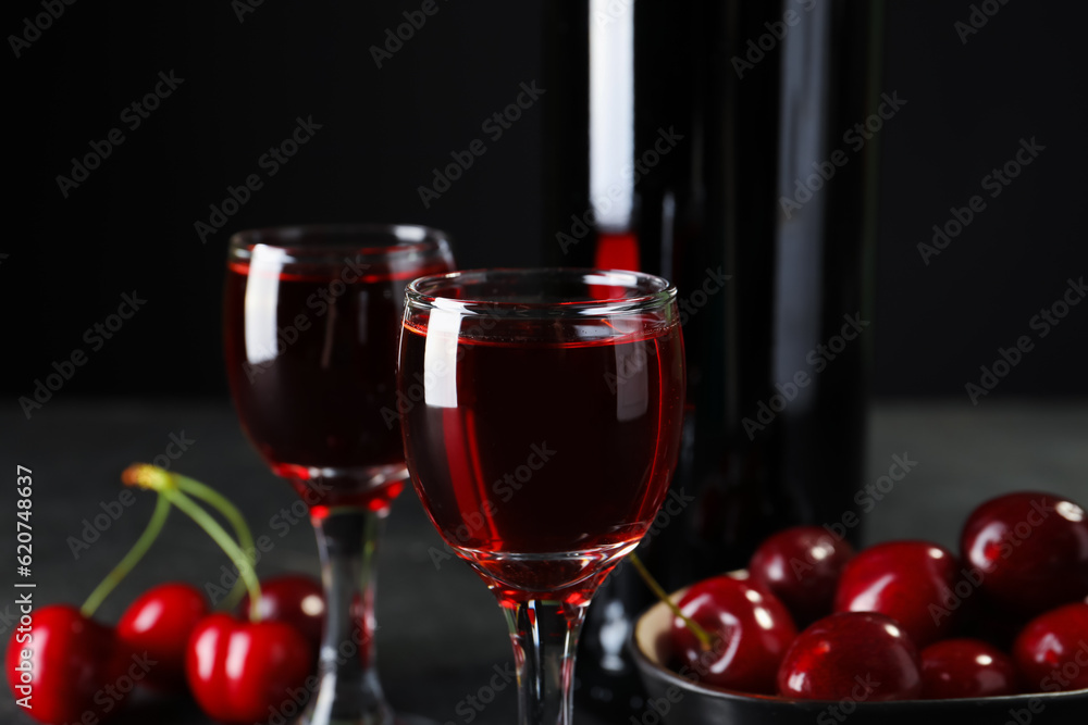 Glasses and bottle with sweet cherry liqueur on black background