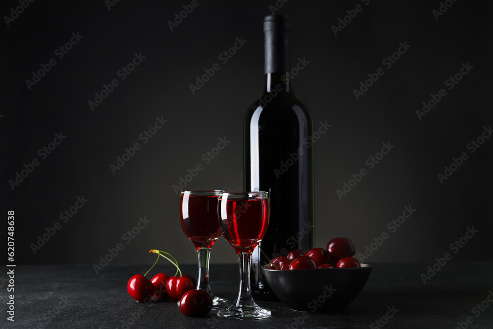 Glasses and bottle with sweet cherry liqueur on black background