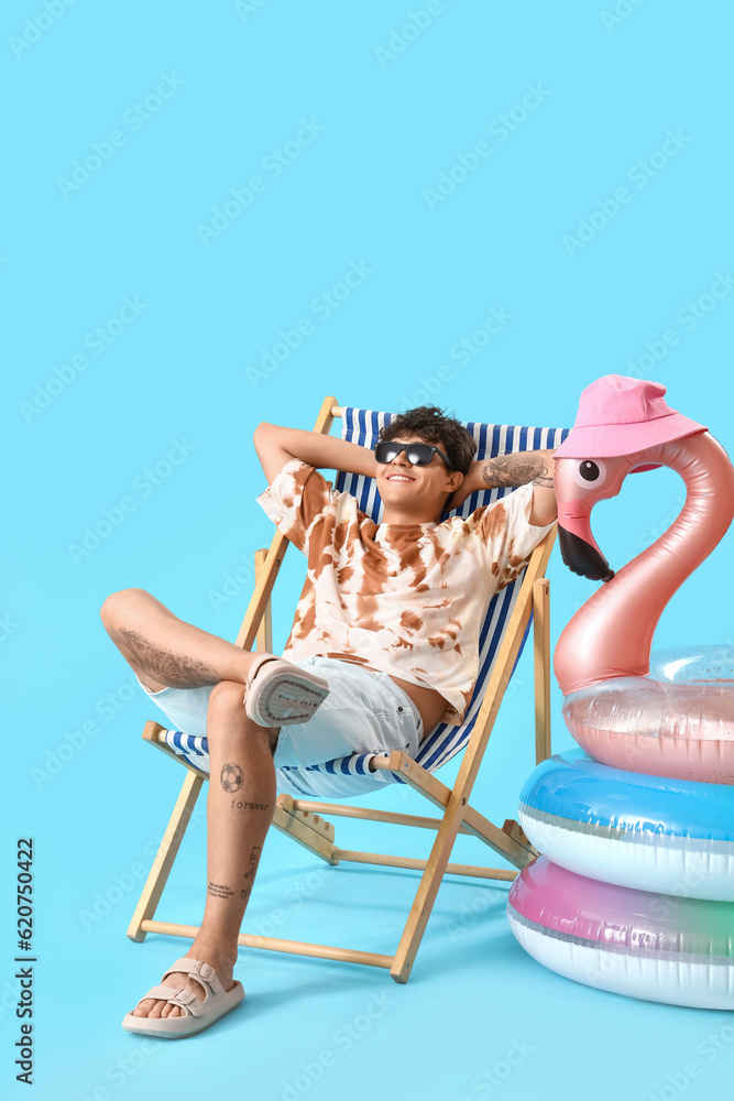 Young man in deck chair and swim rings on blue background