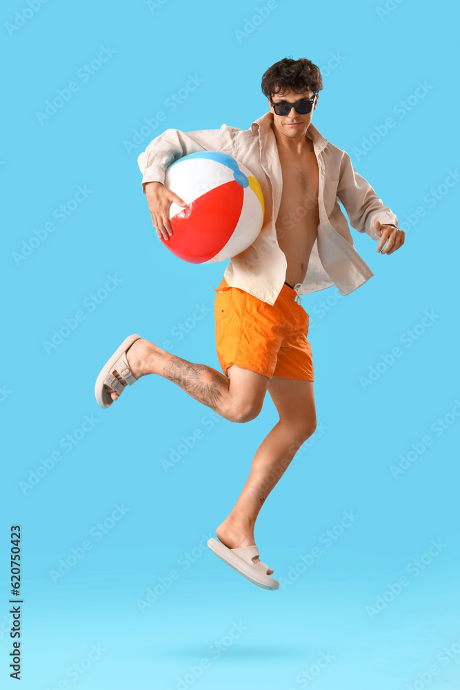 Young man with beach ball jumping on blue background