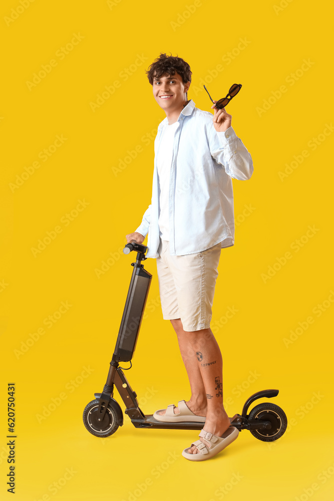 Young man with sunglasses and electric scooter on yellow background