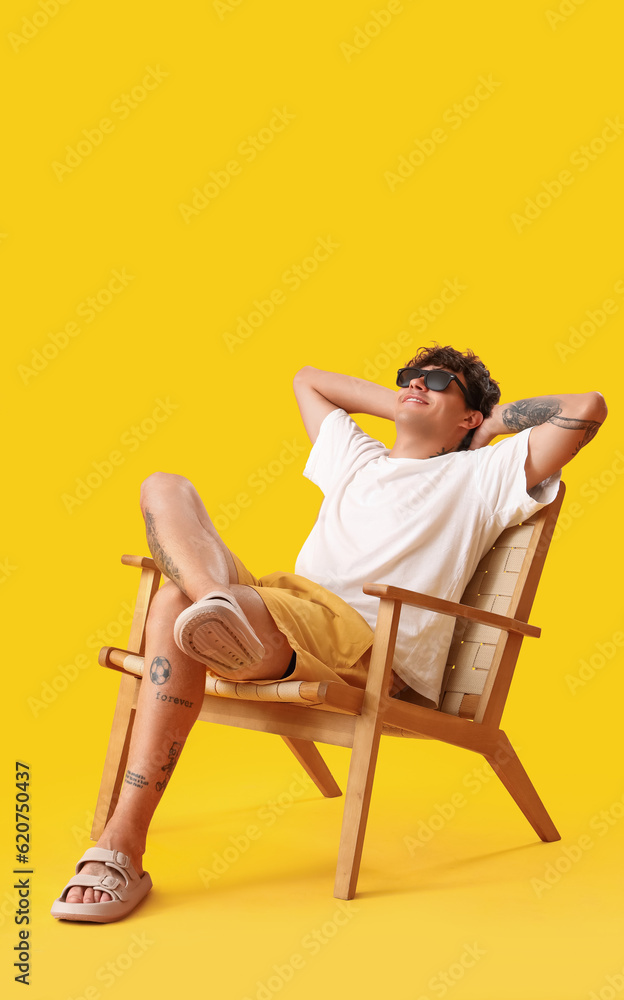 Young man resting in chair on yellow background