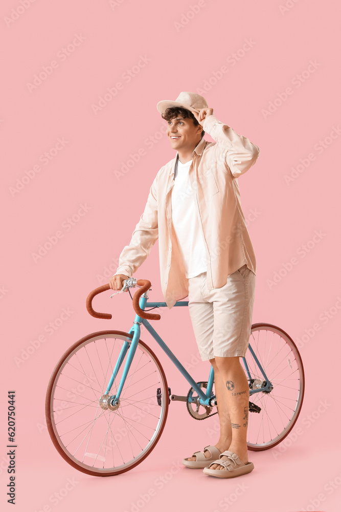 Young man in summer hat with bicycle on pink background