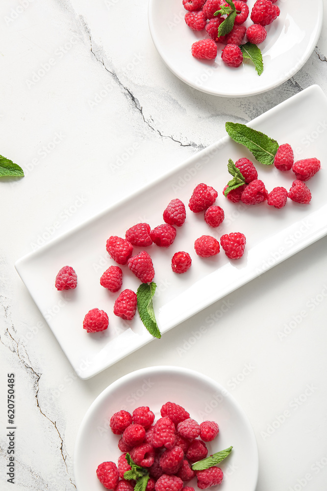 Plates with fresh raspberries and mint on white background