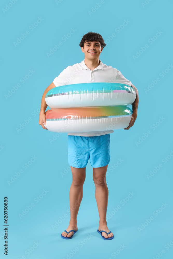 Young man with swim rings on blue background