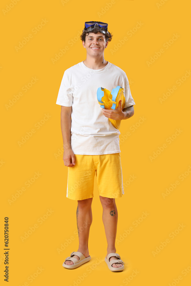 Young man with snorkeling mask and flippers on yellow background