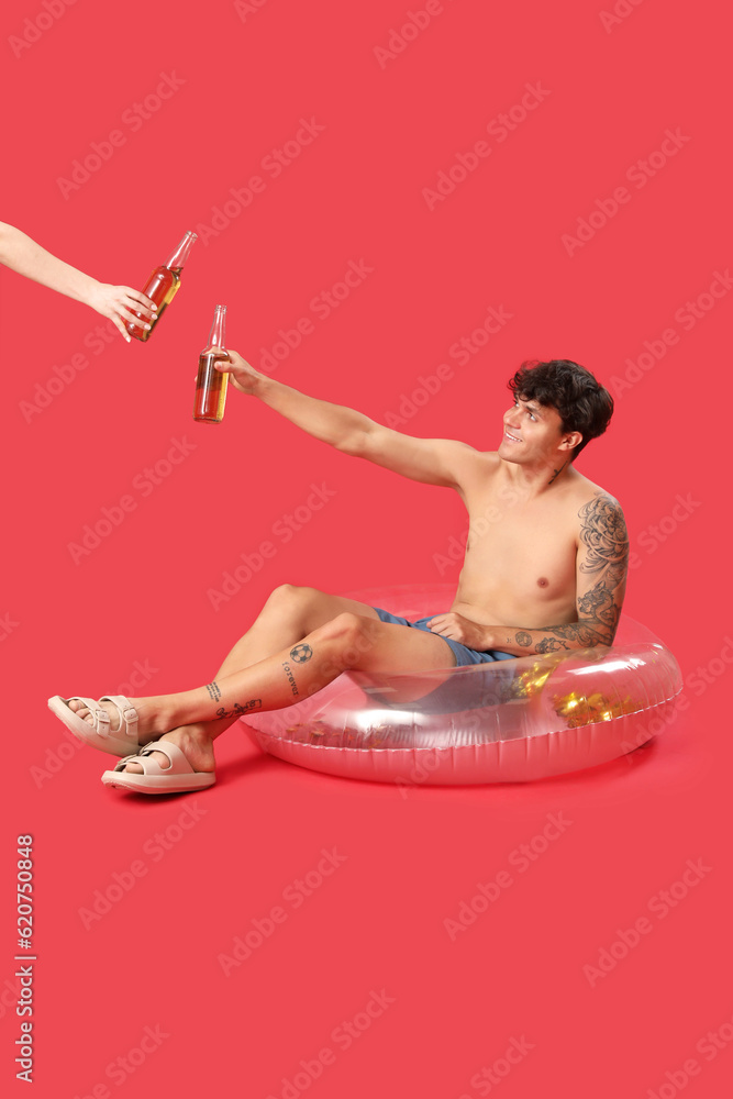 Young man with swim ring and beer on red background