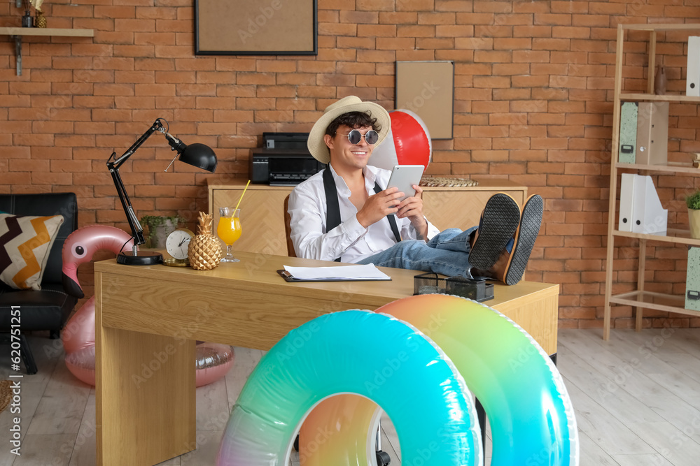 Young businessman with tablet computer ready for summer vacation in office