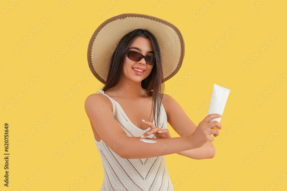 Beautiful young woman applying sunscreen cream on yellow background