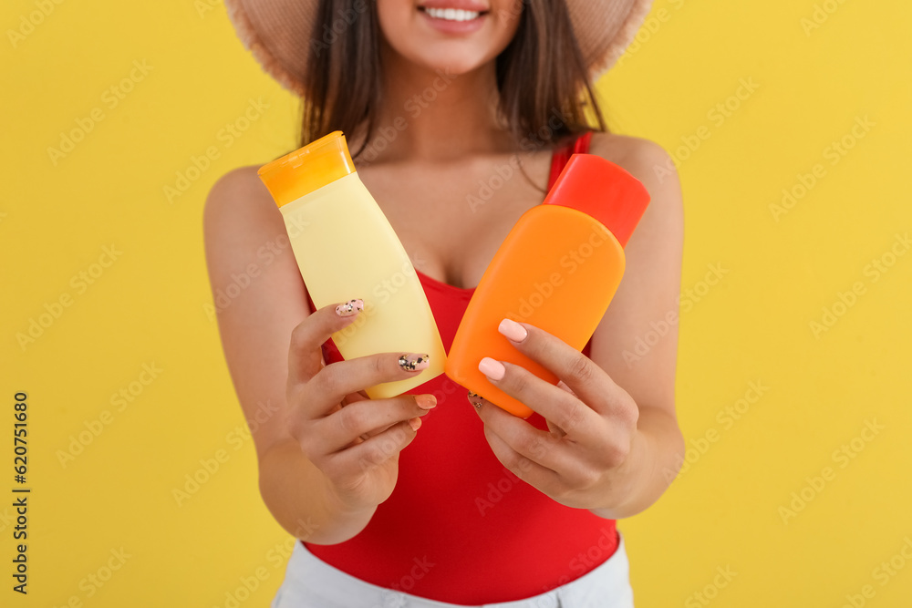 Beautiful woman with bottles of sunscreen cream on yellow background, closeup