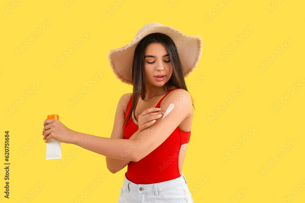 Beautiful young woman applying sunscreen cream on yellow background