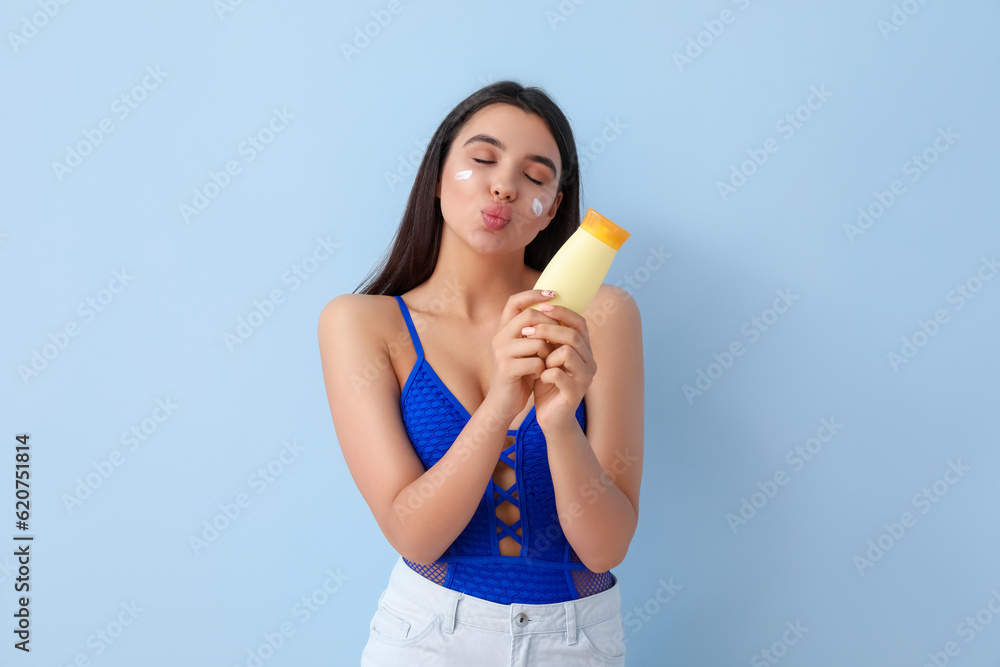 Beautiful young woman with sunscreen cream blowing kiss on light background