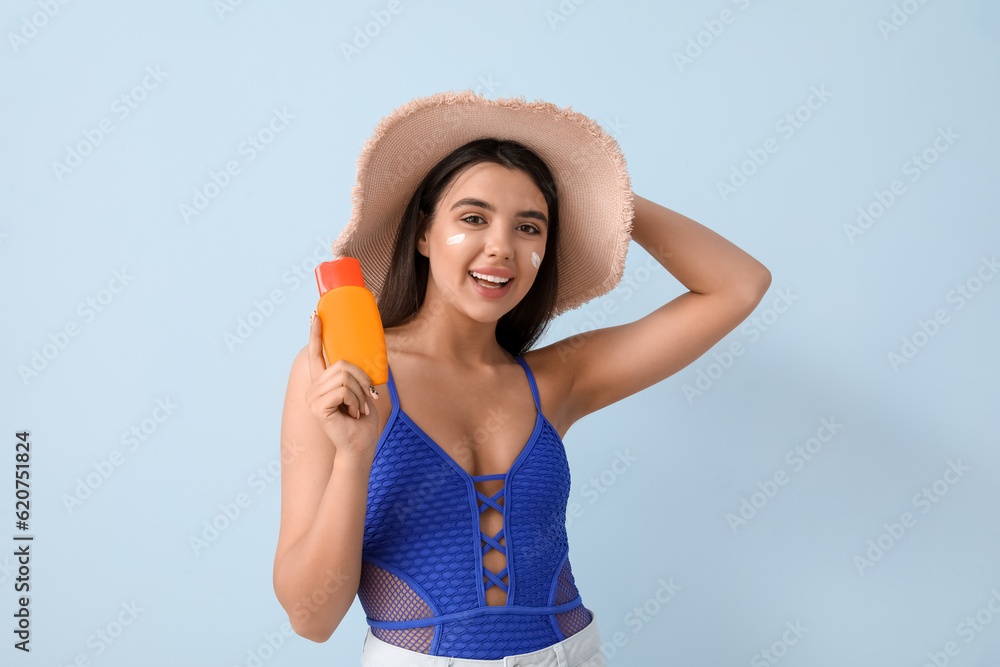 Beautiful young woman with sunscreen cream on light background