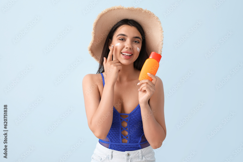 Beautiful young woman with sunscreen cream on light background