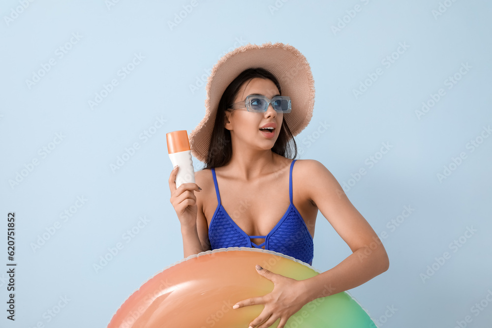 Beautiful young woman with sunscreen cream and swim ring on light background