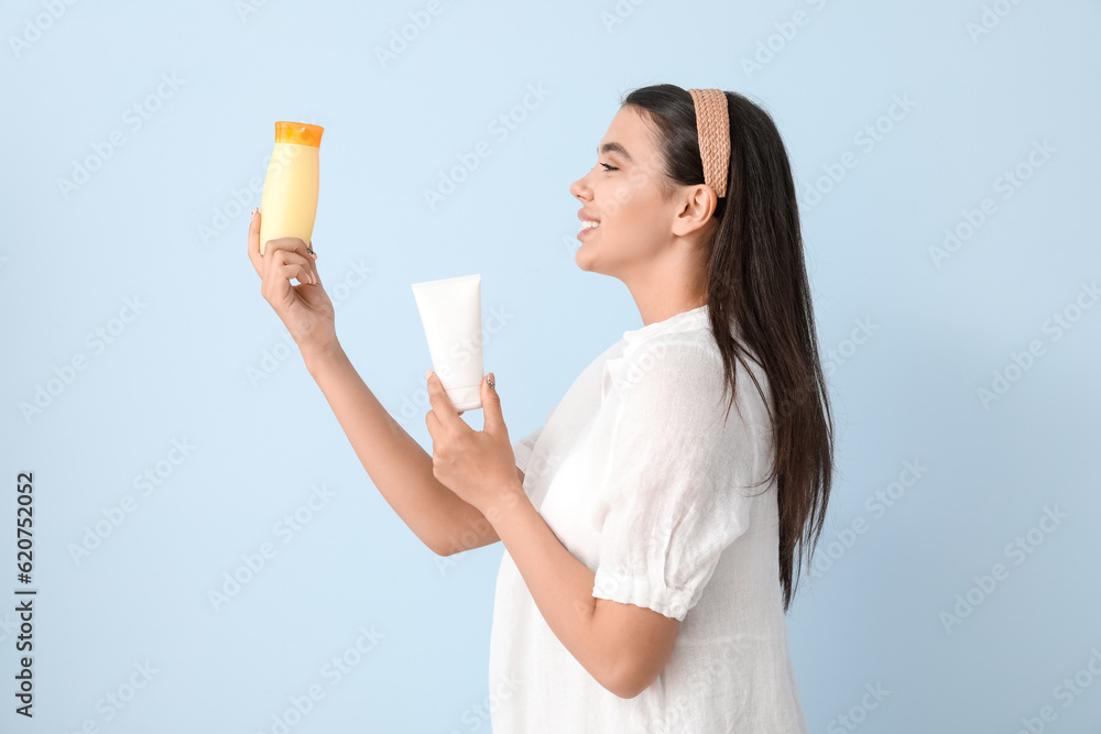 Beautiful young woman with bottles of sunscreen cream on light background