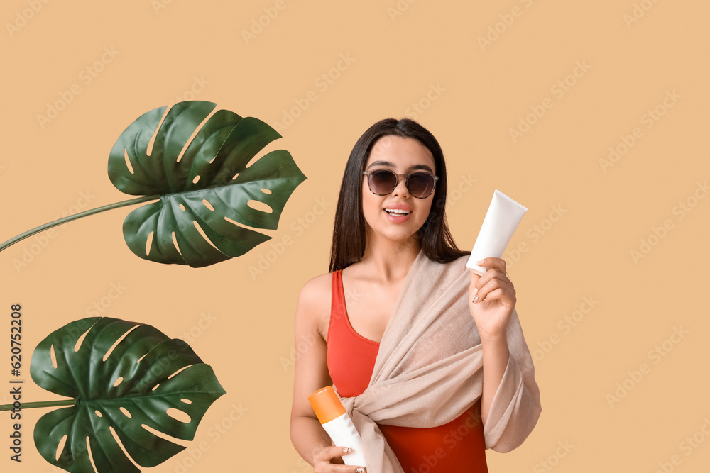 Beautiful woman with bottles of sunscreen cream and palm leaves on beige background