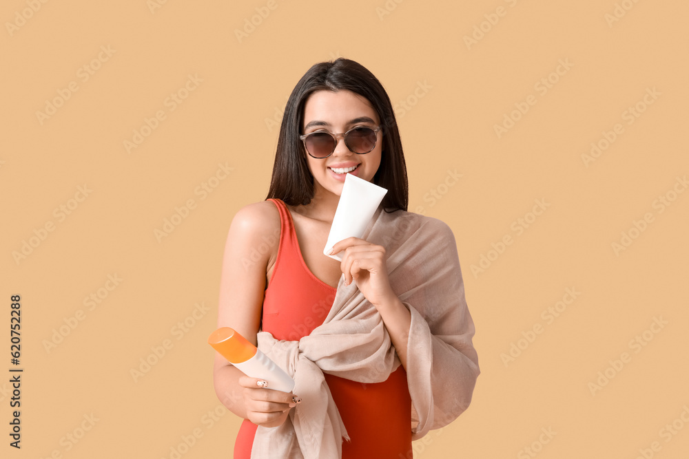 Beautiful woman with bottles of sunscreen cream on beige background