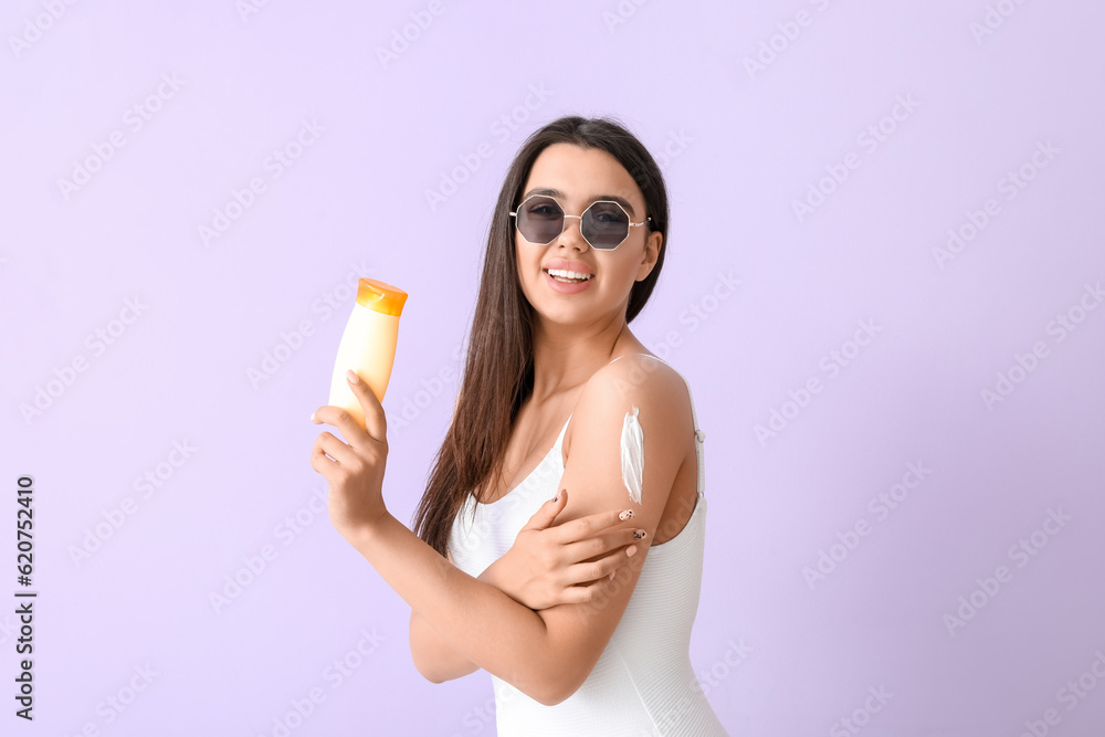 Beautiful young woman with sunscreen cream on lilac background