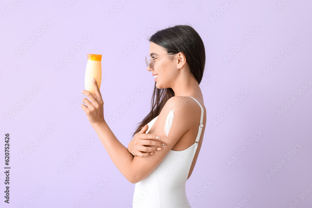 Beautiful young woman with sunscreen cream on lilac background