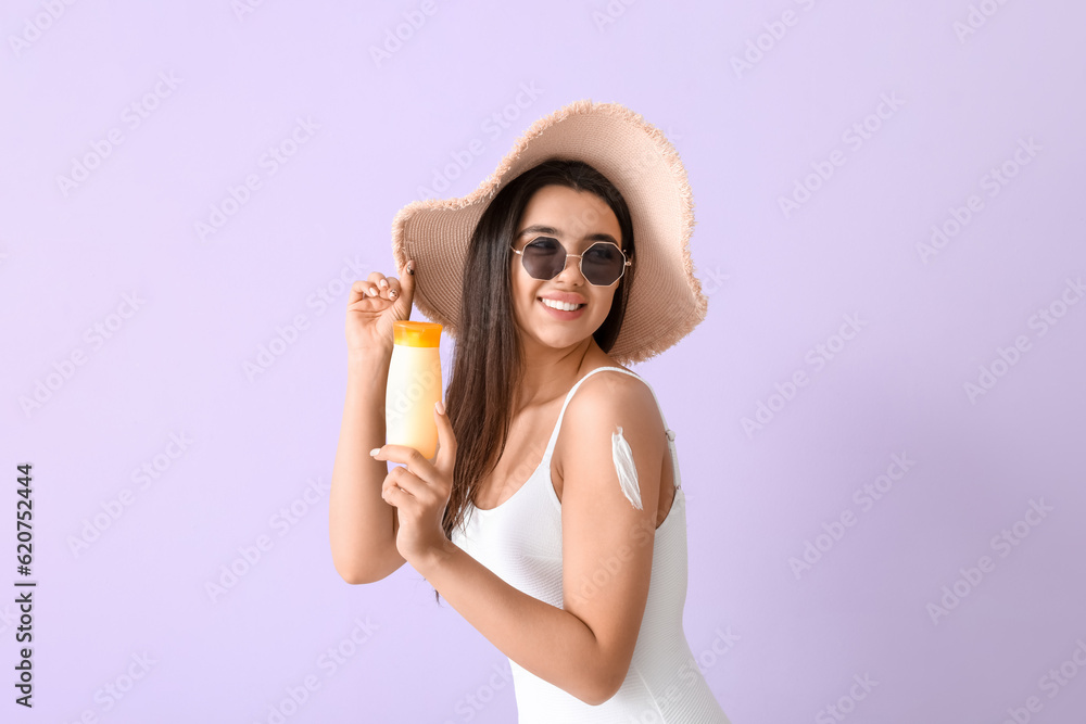 Beautiful young woman with sunscreen cream on lilac background