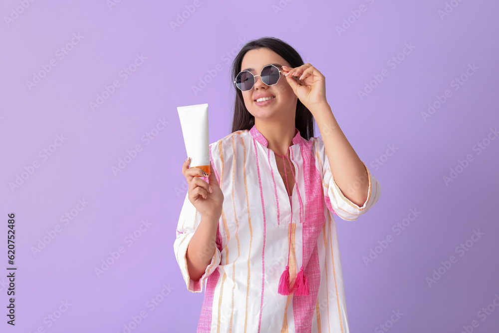 Beautiful young woman with sunscreen cream on lilac background