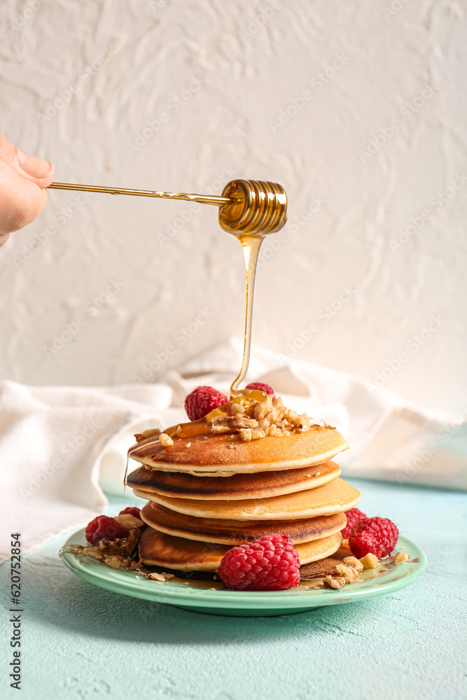 Adding honey onto tasty pancakes with raspberries on light background