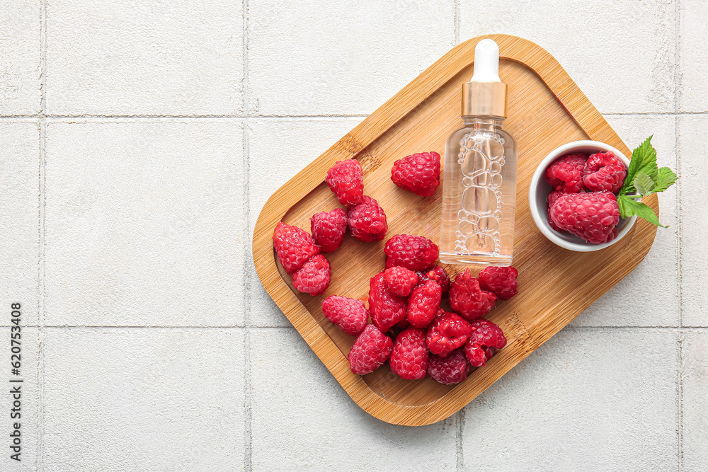 Wooden board with bottle of cosmetic raspberry oil on white tile background