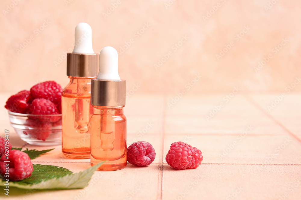 Bottles of cosmetic raspberry oil and bowl with berries on pink tile table