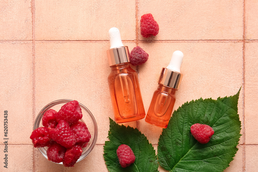 Bottles of cosmetic raspberry oil and bowl with berries on pink tile table