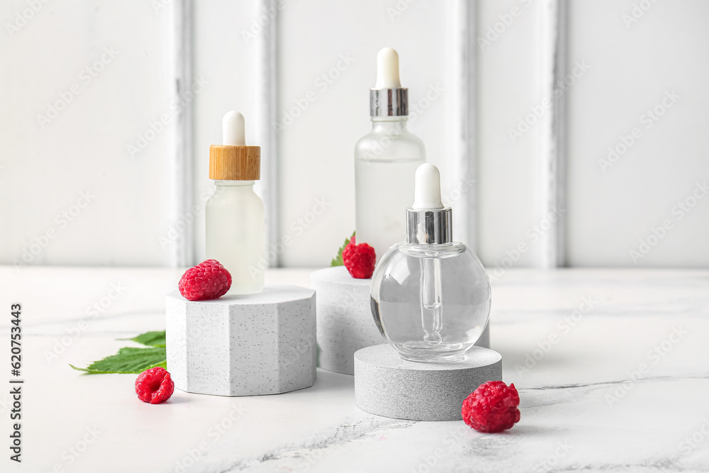 Decorative podiums with bottles of cosmetic raspberry oil on white background